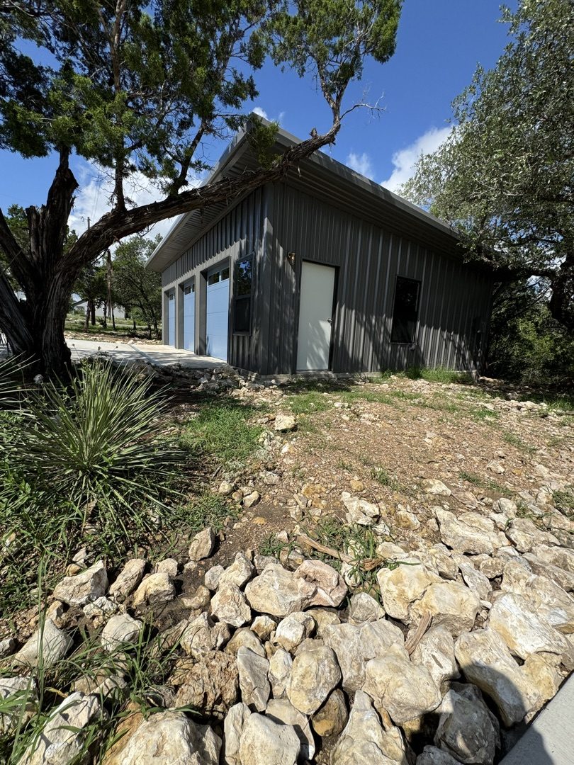 Gray metal garage framed by cedar trees, Canyon Lake metal building